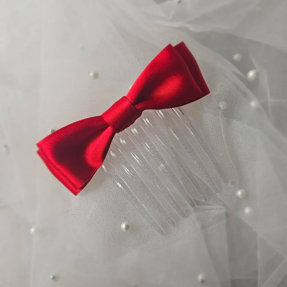 Red satin ballet exam bow on a clear hair comb, designed for classical ballet examinations