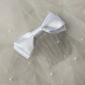 White satin ballet exam bow on a clear hair comb, designed for classical ballet examinations