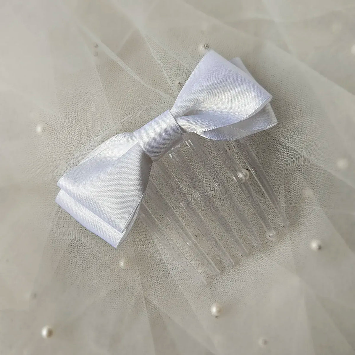 White satin ballet exam bow on a clear hair comb, designed for classical ballet examinations