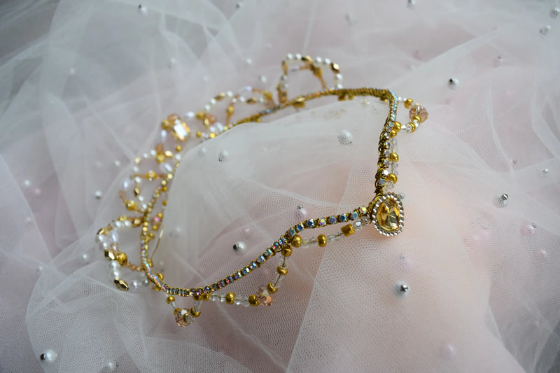 Gold tiara with gemstones on a white fabric background
