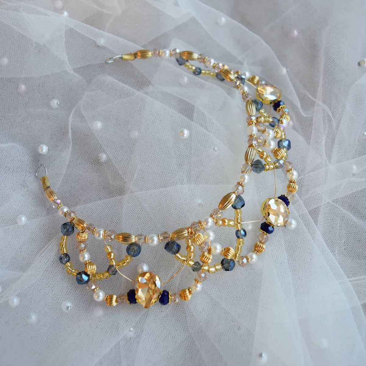 Beaded tiara with gold, blue, and white beads on a sheer fabric background