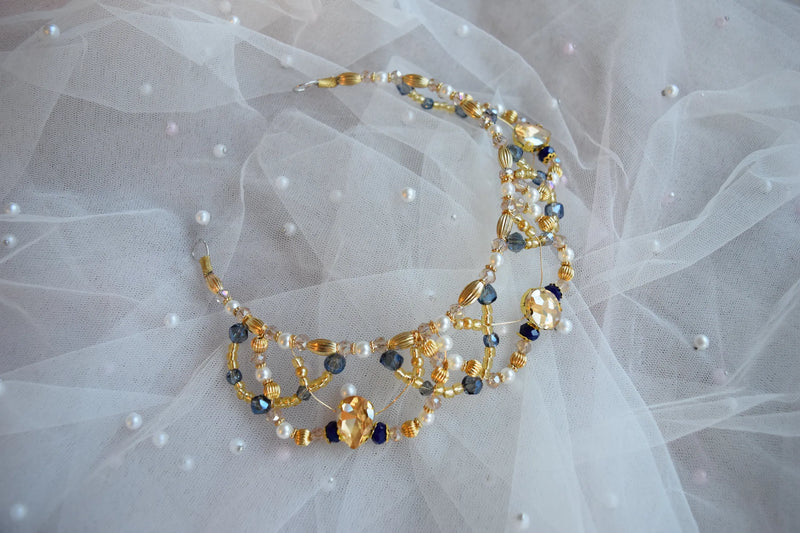 Tiara headpiece with gold and blue beads on a white fabric background